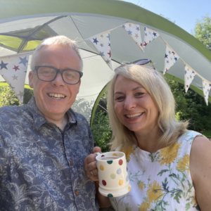 Simon and Gill with a mug of coffee under a tent with bunting