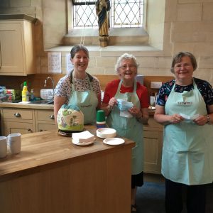 Three smiling ladies in the church kitchen wearing aprons