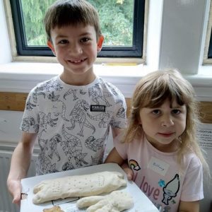 Children holding pottery in the shape of dinosaur bones ready for the kiln