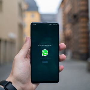 Hand holding a mobile phone with the WhatsApp title screen showing