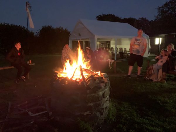 Members of the church gathered around the campfire in the dusk