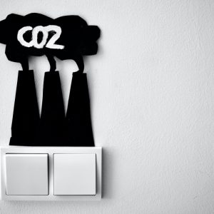 Two light switches with a chalk board in the shape of chimneys giving out smoke about it. The words CO2 are written in chalk on the smoke